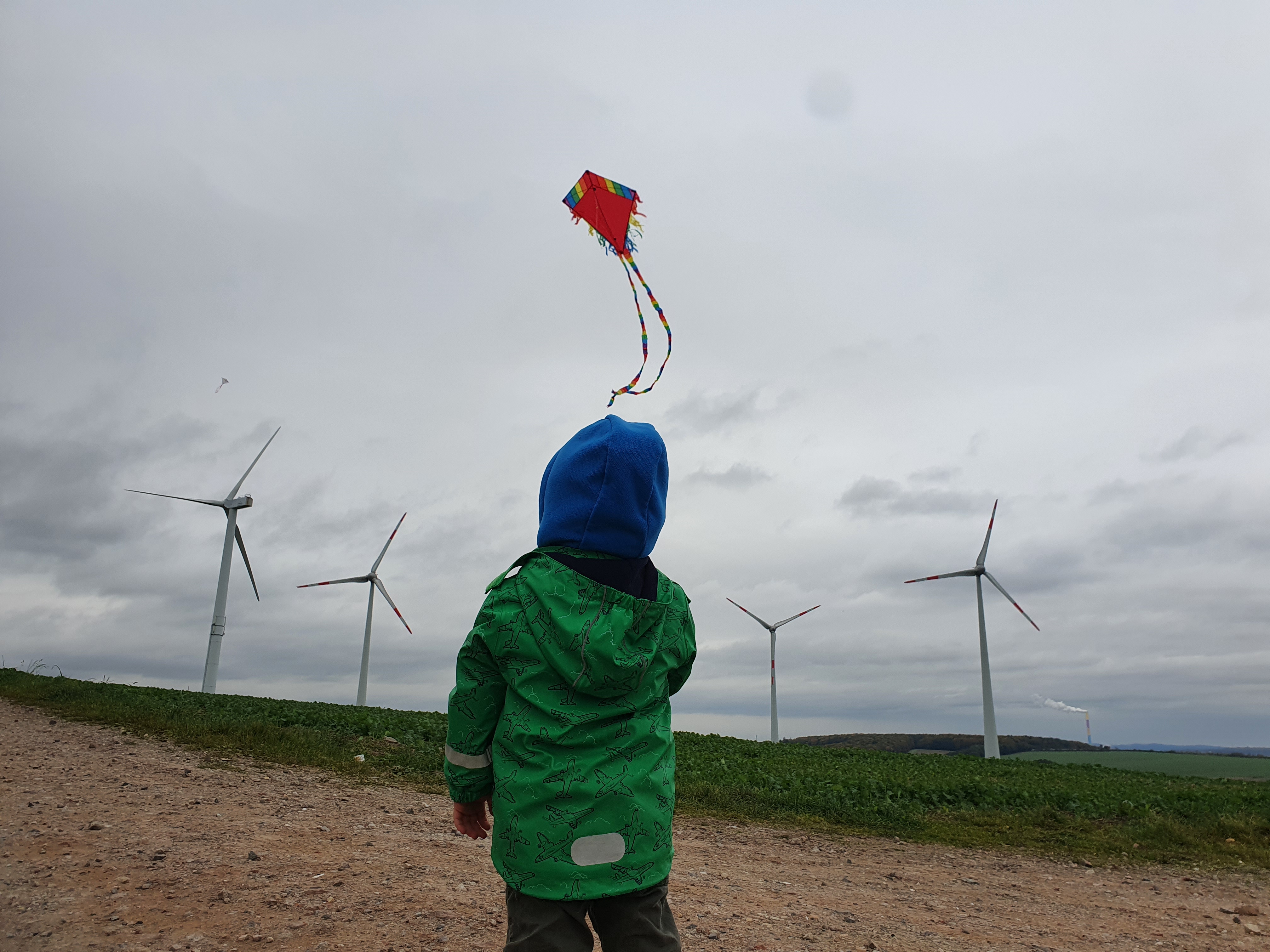 Kind lässt Drachen steigen, im Hintergrund Windräder