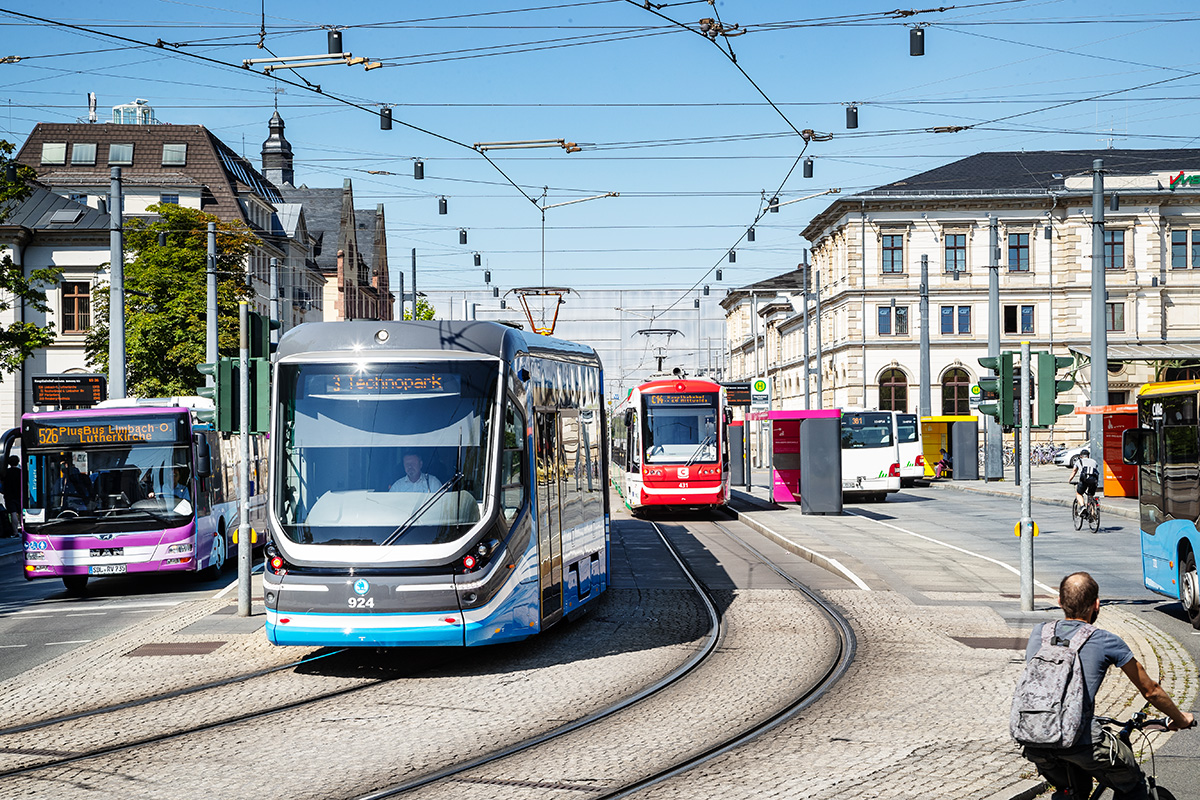 Im Bild zu sehen ist der Hauptbahnhof Chemnitz mit einer Straßenbahn, einer Citybahn, mehreren Bussen und einem Fahrradfahrer im Vordergrund.