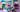 Das Bild zeigt die drei Trampolinkünstler der belgischen Gruppe TnT während eines Auftritts vor einer bunten Bühne. Sie tragen Hawaii-Hemden in Grün, Rot und Blau. Einer von ihnen hält einen rot-weiß gestreiften Rettungsring, während ein anderer durch den Ring springt. Rechts im Bild sieht man unscharf und von hinten eine komplett in Lila gekleidete Person mit einem Hut. Das Wetter ist schön.